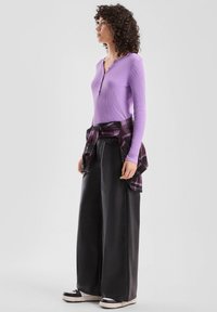 Fioletowy prążkowany top z długim rękawem o kroju henley, zestawiony z szerokimi czarnymi spodniami i przewiązaną czarno-fioletową koszulą w kratę. Czarne sneakersy.