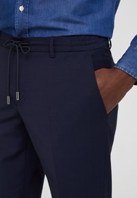 Pantalones azul marino con una textura suave, cinturilla elástica y cordón ajustable. Bolsillo lateral con un corte limpio y costura reforzada.