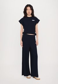 Tamno plavi rebrasti pleteni crop top s kratkim rukavima, uparen s hlačama širokih nogavica. Oba komada imaju minimalistički dizajn i mekani tekstur.
