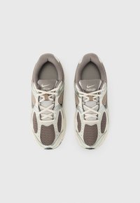 Grå og beige Nike-sneakers med mesh-stoff, reflekterende detaljer og en polstret såle. Har runde snører og en polstret krage.