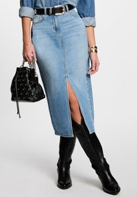 Denim rok met een split aan de voorkant, middelmatige wassing, gestructureerde pasvorm, gecombineerd met zwarte kniehoge laarzen en een gequilt zwarte handtas.