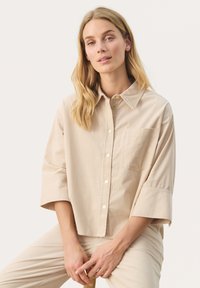 Beige korduroy košile s límečkem, dlouhými rukávy a náprsní kapsou. Má knoflíky v kontrastní barvě a design s volným střihem.