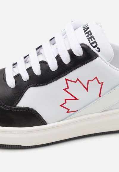 Zapatillas en blanco y negro con un diseño elegante, que presentan un gráfico de una hoja de arce roja, cordones blancos y una suela de goma texturizada.