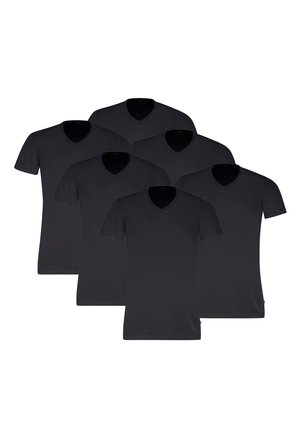 Mann trägt ein eng anliegendes schwarzes V-Ausschnitt-T-Shirt mit kurzen Ärmeln und hellgraue Boxershorts, steht vor einem einfarbigen Hintergrund.