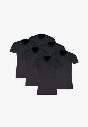 Mann trägt ein eng anliegendes schwarzes V-Ausschnitt-T-Shirt mit kurzen Ärmeln und hellgraue Boxershorts, steht vor einem einfarbigen Hintergrund.