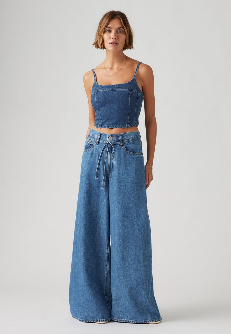 Top en denim cropped avec des bretelles ajustables, associé à un jean taille haute à jambes larges. Les deux en bleu clair, avec une coupe décontractée et un minimum de détails.