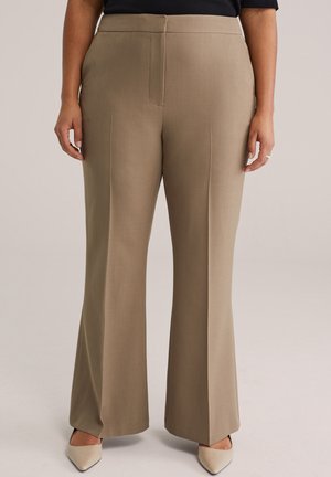 Pantalones beige a medida con diseño de pierna ancha. Presentan una textura suave, costura frontal y cintura a media altura. Combinados con zapatos puntiagudos beige.