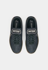 Tenisky Puma z tmavosivej semišovej kože s gumovou podrážkou. Majú zelené šnúrky a výrazný suchý zips. Značenie na jazyku a boku.