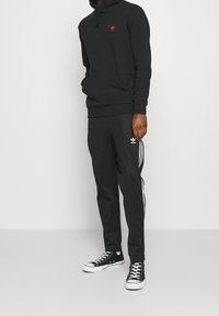 Svart hoodie med röd logga, matchande svarta byxor för träning med vita ränder, och svarta högstövel-sneakers med vita sulor.