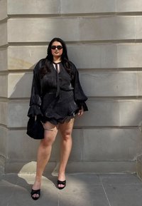 Melns, caurspīdīgs blūze ar balonu piedurknēm un sasienamu apkakli, apģērbta ar kārtainu melnu svārku. Aksesuārs tika pievienots ar mazu melnu rokassomu un sandālēm.