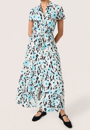 Kukkakuvioinen maksimekko lyhyillä hihoilla, valkoinen pohja, jossa sinisiä ja mustia kukkia, napitus edessä ja kiristetty vyötärö solmittavalla vyöllä.