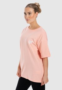 Camiseta de gran tamaño en color rosa claro, con mangas cortas, que presenta un diseño de mariposa blanca en el pecho. Elaborada con suave y transpirable material de algodón.