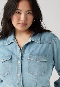 Ανοιχτό μπλε τζιν πουκάμισο με κουμπιά μπροστά, δύο τσέπες στο στήθος και ασημένιες λεπτομέρειες. Διαθέτει κλασικό γιακά και χαλαρή εφαρμογή.