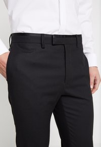 Svarta dressbyxor i texturerat tyg, med rak bendesign, sidofickor och platt front samt ett matchande bälte.