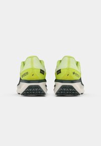 GORE-TEX hardloopschoenen met een felgeel bovenwerk, verstevigde hak en een zwarte geprofileerde loopzool met geometrische patronen voor grip.
