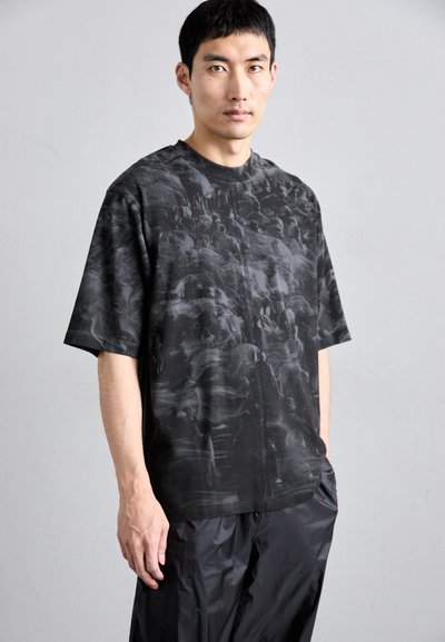 Camiseta negra de manga corta con un patrón abstracto en gris, hecha de un material suave, con un ajuste relajado y cuello redondo.