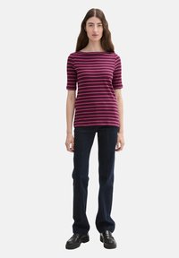 Blandet t-shirt i dyb lilla og pink med bådformet halsudskæring og korte ærmer. Sammen med mørkeblå, vide denim jeans og sorte sko.