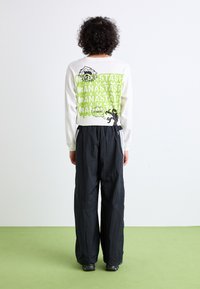 Chemise blanche à manches longues avec impression graphique verte au dos, accompagnée d'un pantalon large noir. Texte et illustrations en évidence.