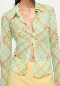 Camicia a bottoni leggera e trasparente in plaid nei colori verde, arancio e bianco. Caratterizzata da un colletto arricciato, maniche lunghe e un design aderente.