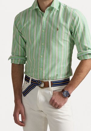Groen gestreept shirt met witte, roze en blauwe lijnen, slim fit ontwerp, met knoopsluiting bij de kraag. Gecombineerd met beige broek en een meerkleurige gestreepte riem.