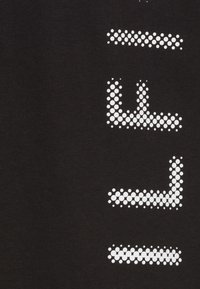 Czarny bawełniany t-shirt z dużym, białym tekstem w kropki na przodzie. Kropki różnią się rozmiarem, tworząc wyraźny wzór wizualny.