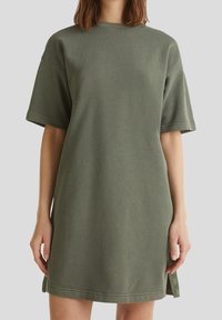 Olive green oversized t-shirt dress with short sleeves, ribbed fabric, round neck, and side slits featuring subtle logo accents.