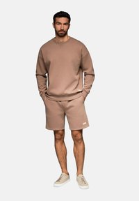 Sweatshirt girocollo in cotone beige abbinato a pantaloni corti coordinati. Sneakers in un beige chiaro, con accenti minimali e un design semplice.
