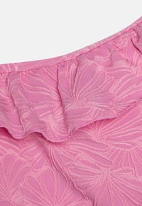 Pink ruffled fabric featuring a floral pattern. The texture appears smooth with raised embroidery, highlighting the flower design.