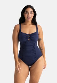 Mornarsko modra enodelna kopalna obleka z izrezom, nagubanimi detajli, širokimi naramnicami in tremi dekorativnimi vodoravnimi trakovi na prsih.
