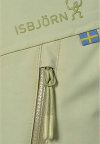 Närbild av en ljusgrön jackdragkedja med ISBJÖRNs varumärke och en liten svensk flagga.