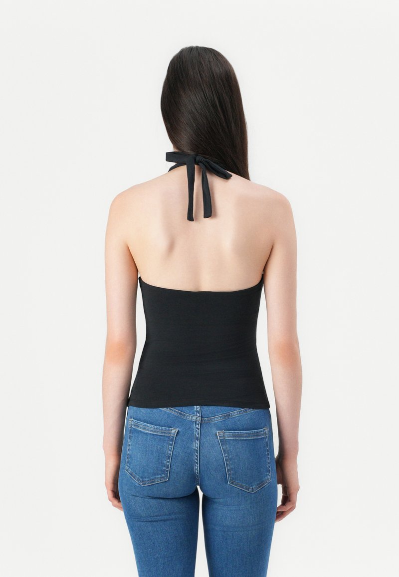Haut halter noir avec un design à nouer à l'arrière, présentant une silhouette ajustée. Associé à un jean en denim bleu, mettant en avant une coupe classique et des poches arrière.