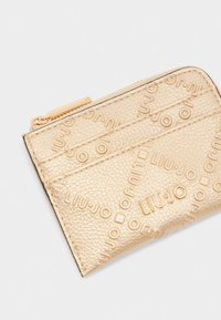 Portafoglio in pelle con texture dorata, caratterizzato da motivi a logo impresso, chiusura con zip e scomparti per schede per un'organizzazione ottimale. Forma rettangolare compatta.