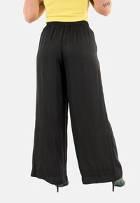 Pantalones anchos negros con cinturilla elástica, tejido ligero, textura suave y longitud recortada, combinados con zapatos de tacón alto.