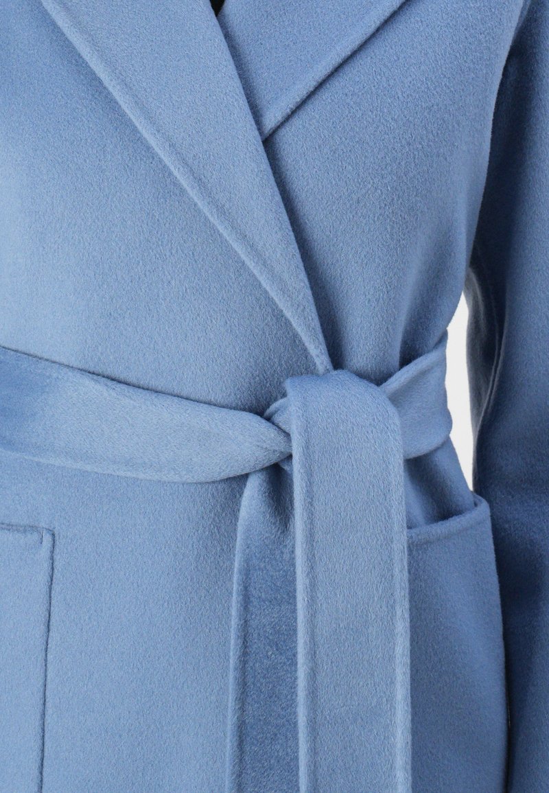 Helles Blau, weicher Fleece-Mantel mit breitem Revers, tailliertem Gürtel und aufgesetzten Taschen. Der Stoff hat eine glatte, strukturierte Oberfläche.