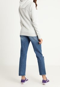 Sudadera con capucha gris de corte relajado, combinada con jeans de pierna recta azules y zapatillas moradas con acentos blancos.
