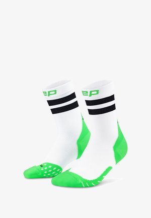 Socks sportivi bianchi con strisce nere in alto e dettagli verdi. Presentano una suola verde testurizzata e un logo verde.