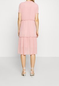 Różowa, warstwowa sukienka midi wykonana z lekkiego, teksturowanego materiału. Posiada krótkie rękawy i pofałdowane szwy. Połączona z białymi sandałkami na obcasie z paskami.