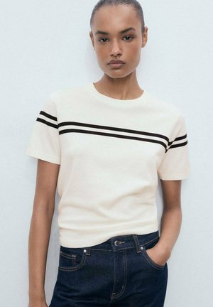 Creme korte mouwen T-shirt met zwarte horizontale strepen, ronde hals, en zachte textuur, gecombineerd met donkere spijkerbroek.