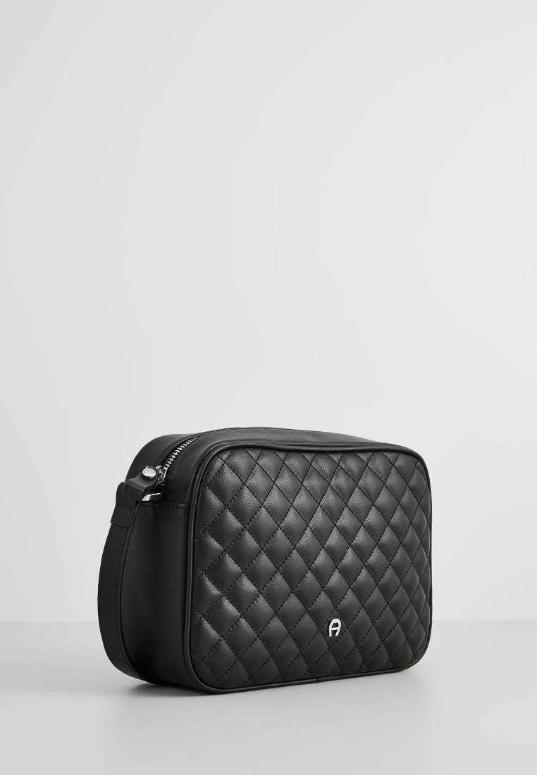 Schwarze, gestepptes Kunstledertasche in rechteckiger Form, mit silberner Hardware und einem Logo-Akzent auf der Vorderseite. Mit Reißverschluss an der Oberseite.