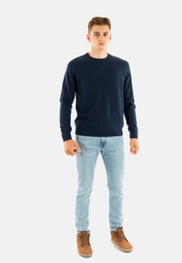 Maglione lavorato a maglia blu scuro con colletto a girocollo, vestibilità slim. Indossato con jeans azzurri e stivali marroni stringati per un look casual.