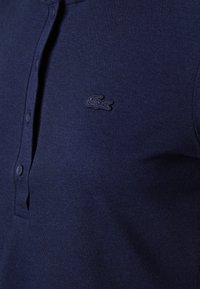 Námořnická polo košile vyrobená z texturované tkaniny s tříknoflíkovým zapínáním. Obsahuje malé vyšívané logo na levém horním prsu.