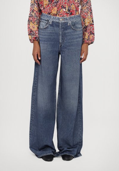 Bredde jeans i mørkeblå denim. Med høj talje, fem-lomme design og rå kant. Matchet med en mønstret langærmet top.