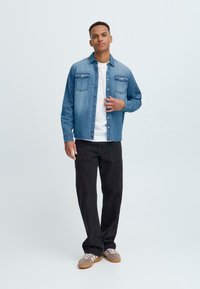 Denim shirt in light blue, featuring two chest pockets, button placket, and long sleeves, paired with black pants and gray sneakers.