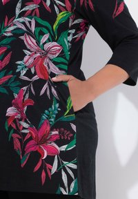 Czarna tunika z żywym kwiatowym haftem w kolorach różowym, czerwonym, białym i zielonym. Projekt zawiera boczną kieszeń i luźny krój.