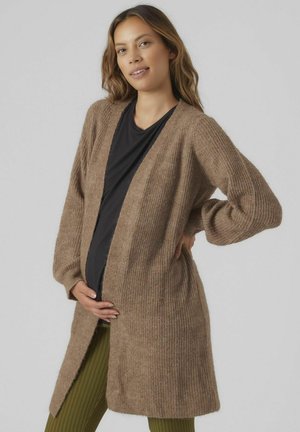 Cardigan marrone a coste con maniche lunghe e apertura frontale. Texture morbida, lunghezza fino al ginocchio, indossato sopra a un top nero e pantaloni verdi a coste.