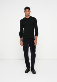 Czarna, długosleeve'owa koszulka polo z zapięciem na guziki, zestawiona z granatowymi spodniami z sztruksu. Model nosi czarne skórzane buty. Prosty design i dopasowanie.