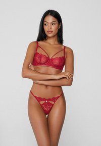 Red lace lingerie set featuring a bra with underwire and strappy design, paired with matching thong showcasing cut-out details and floral patterns.