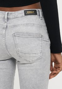 Γκρι τζιν από ντένιμ με κλασική γραμμή, σχεδίαση με πέντε τσέπες και μαύρη ετικέτα με το όνομα της μάρκας "ONLY" στη μέση.