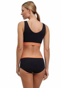 Zwarte sportbra en bijpassende broek met een oranje tailleband. Glad materiaal, aansluitend ontwerp en racerback stijl van de top.