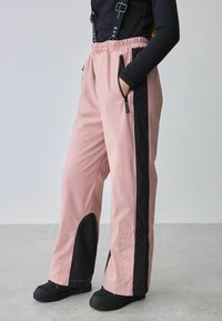 Rausvaičiai ir juodi atsparūs vandeniui kelnių su elastiniu juosmeniu, užtrauktuko kišenėmis, šoninėmis juostelėmis ir iškilmingu "BAKER" ženklu ant kojos.